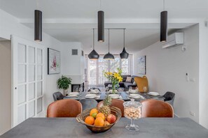 Ein Essbereich mit einem für vier Personen gedeckten Tisch, Pendelleuchten an der Decke und Blick auf das Wohnzimmer.