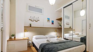 Quarto de hotel com cama, mesas de cabeceira, espelho e janela.