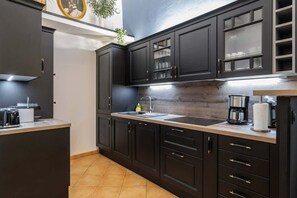Cozinha moderna com armários escuros, bancada de madeira e cafeteira à mostra.