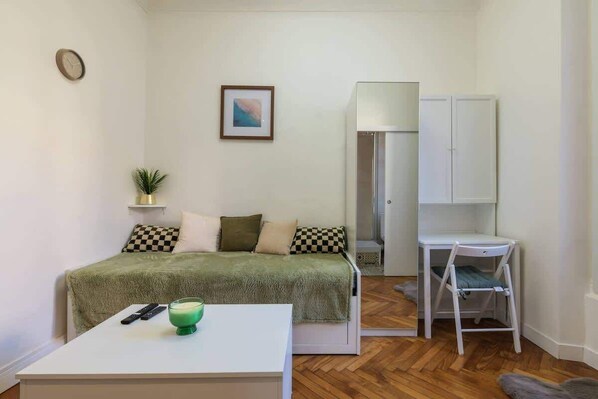 A small, neatly arranged room with a bed, a desk, a chair, a small table, a clock, a framed picture, and a potted plant. - Cozy studio in a beautiful listed residence (Nice)