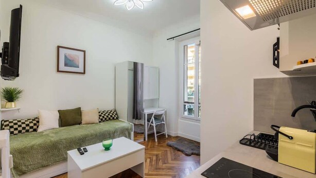 En kompakt opholdsstue med sofa, et lille bord, et tekøkken og et vindue.