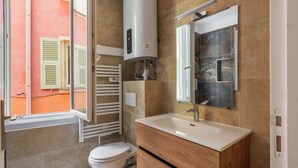A bathroom with a toilet, sink, mirror, and a wall-mounted heater. - Cozy apartment in the heart of the old town (Nice)