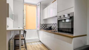 A compact kitchen with white cabinetry, a built-in oven, and a dining area with a table and chairs. - Cozy apartment in the heart of the old town (Nice)