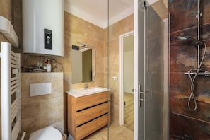 Un baño moderno con cabina de ducha de vidrio, tocador de madera y calefacción integrada.