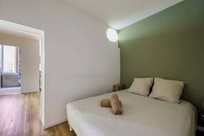 Un dormitorio con cama, almohadas, una mesita de noche y una lámpara de pared.