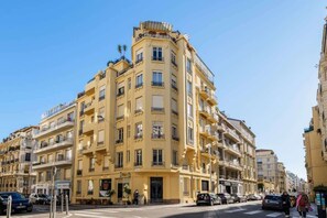 Un edificio de varios pisos con balcones, entrada a nivel de calle y cielo despejado.
