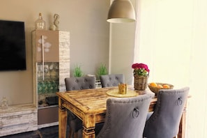 Ein Essbereich mit Holztisch, grau gepolsterten Stühlen, einer Blumenvase und einer Orangenkörbchen.