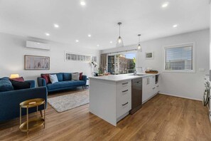 A modern kitchen with a central island, white cabinetry, and a dining area with a blue sofa. - Hamilton Lake Haven - Great Location (Hamilton)