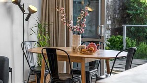 Et spiseområde med et rundt bord, sorte stole, en vase med blomster, en tepotte og en lampe.