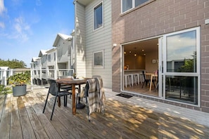 A deck with a table and chairs, a potted plant, and a building with a brick facade and large windows. - Hamilton Lake Haven - Great Location (Hamilton)