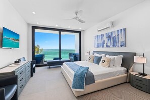 A modern bedroom with a large bed, a desk, and a view of the ocean.
