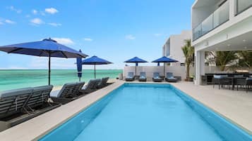 Un espace piscine doté de chaises longues et de parasols, une vue dégagée sur l’océan et une architecture de bâtiment moderne.