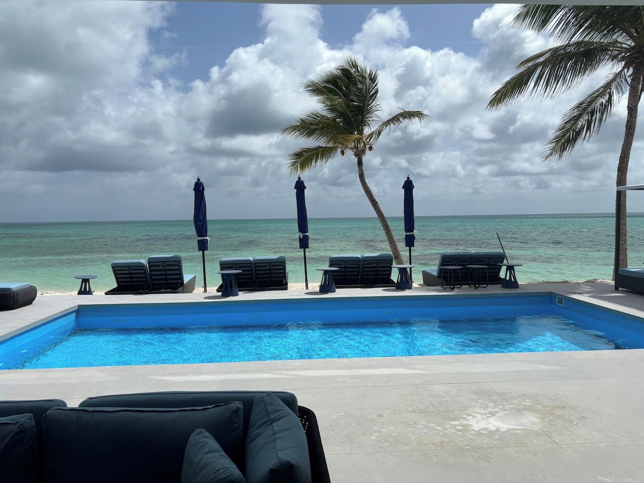 Ein Poolbereich mit Liegestühlen und Sonnenschirmen mit Blick auf einen Strand und den Ozean.