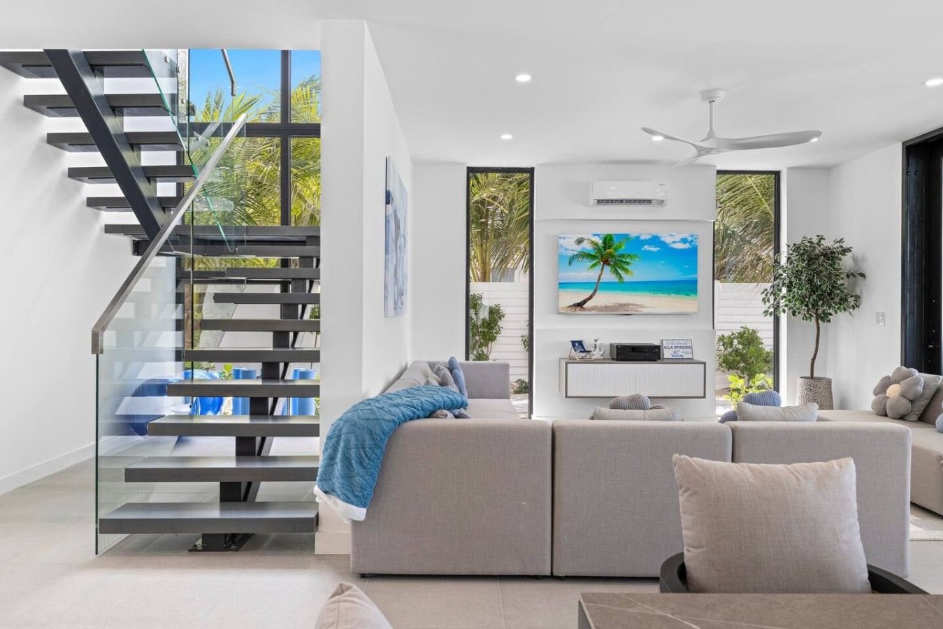 A modern living room with a staircase, a large sofa, a flat-screen TV, and a ceiling fan.