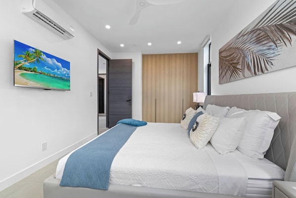 A modern bedroom with a bed, a painting, a ceiling fan, and a door leading to another room.