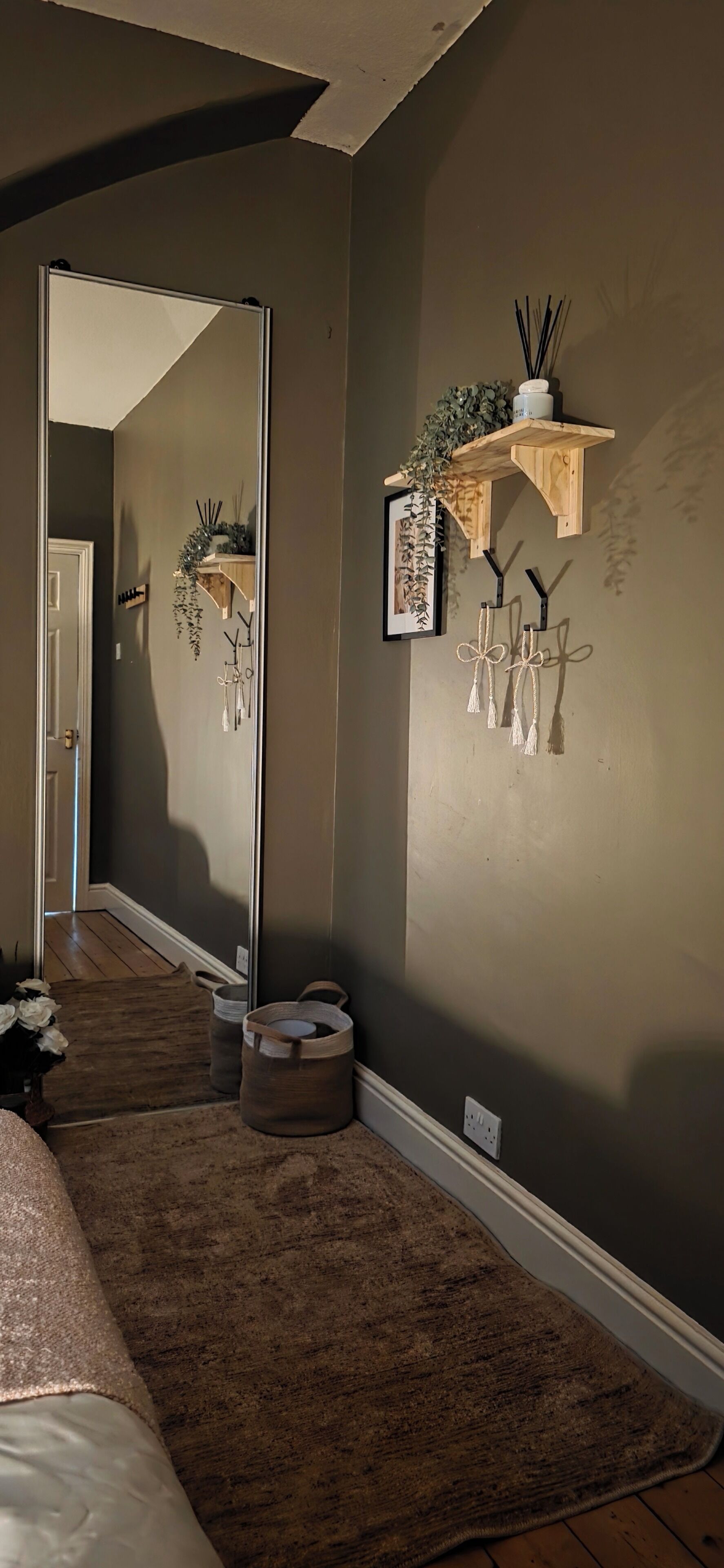 Una habitación con un espejo grande, una estantería de madera con plantas, un adorno colgante y una alfombra.