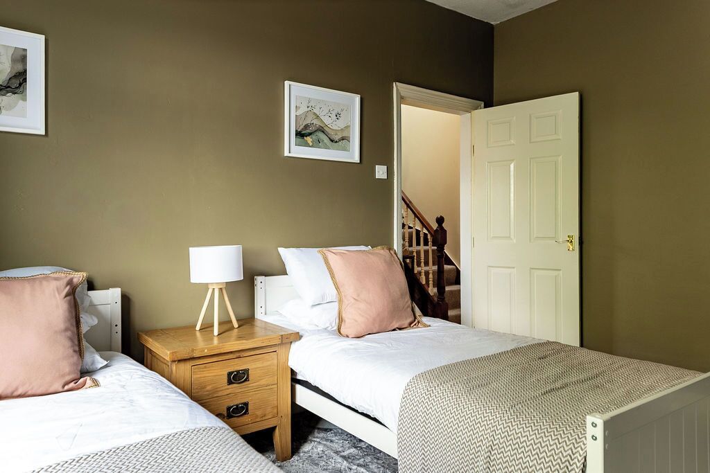 A bedroom with two beds, a nightstand, a lamp, and a framed picture on the wall.