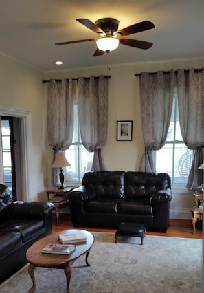 A living room with a ceiling fan, a black leather sofa, a wooden coffee table, and a patterned rug.