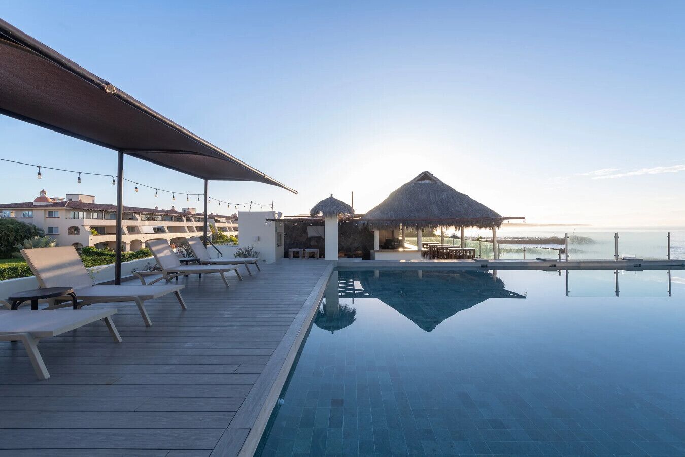 An infinity pool with lounge chairs and a thatched-roof structure.