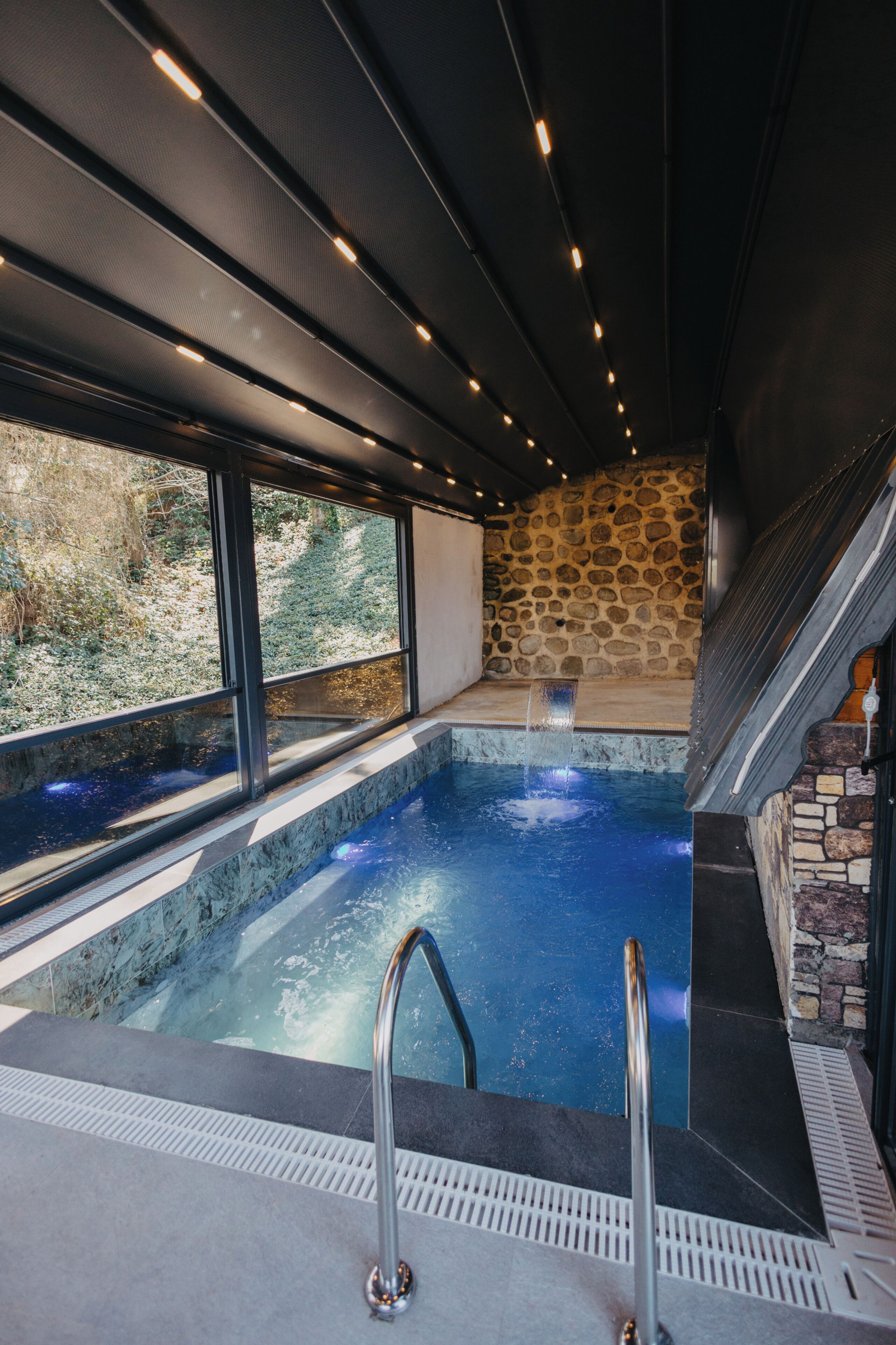 A hot tub with a stone wall and a window overlooking a natural landscape.