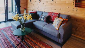 A cozy room with a sofa, a small table with flowers, a patterned rug, and wooden walls.