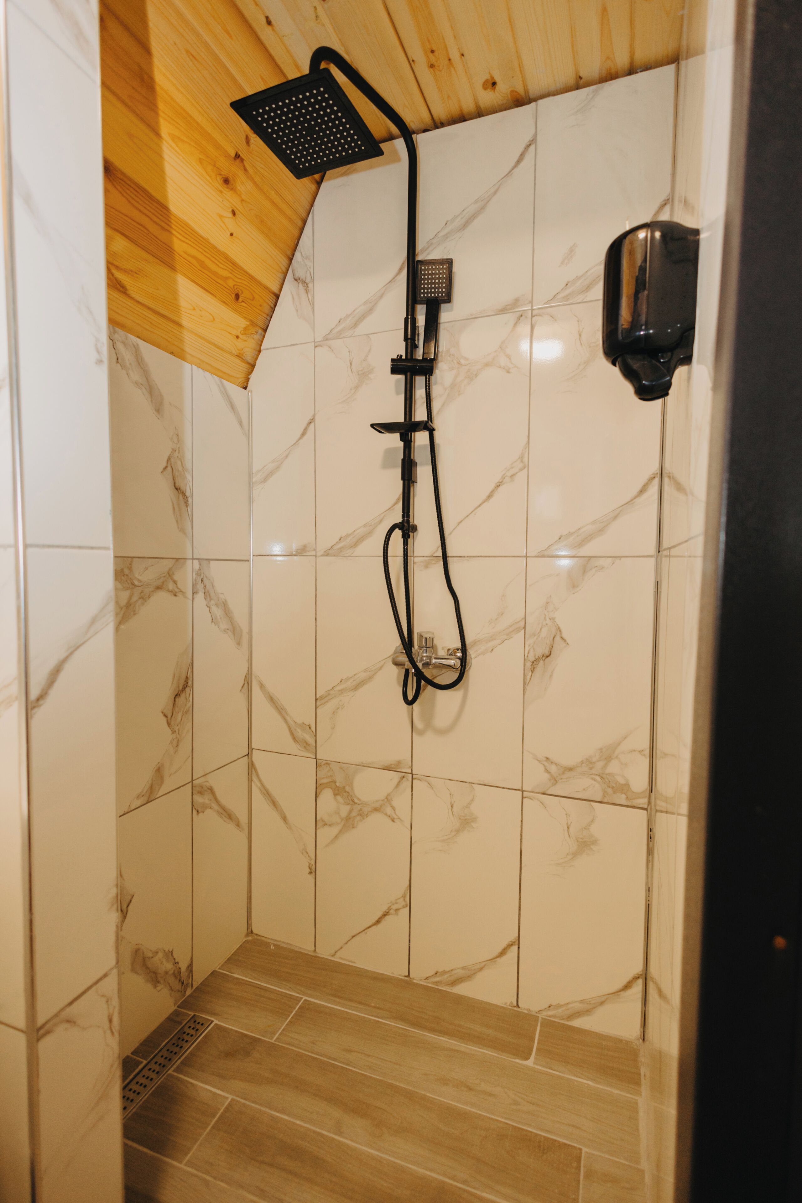 A shower with a wooden ceiling, marble tiles, and a handheld showerhead.