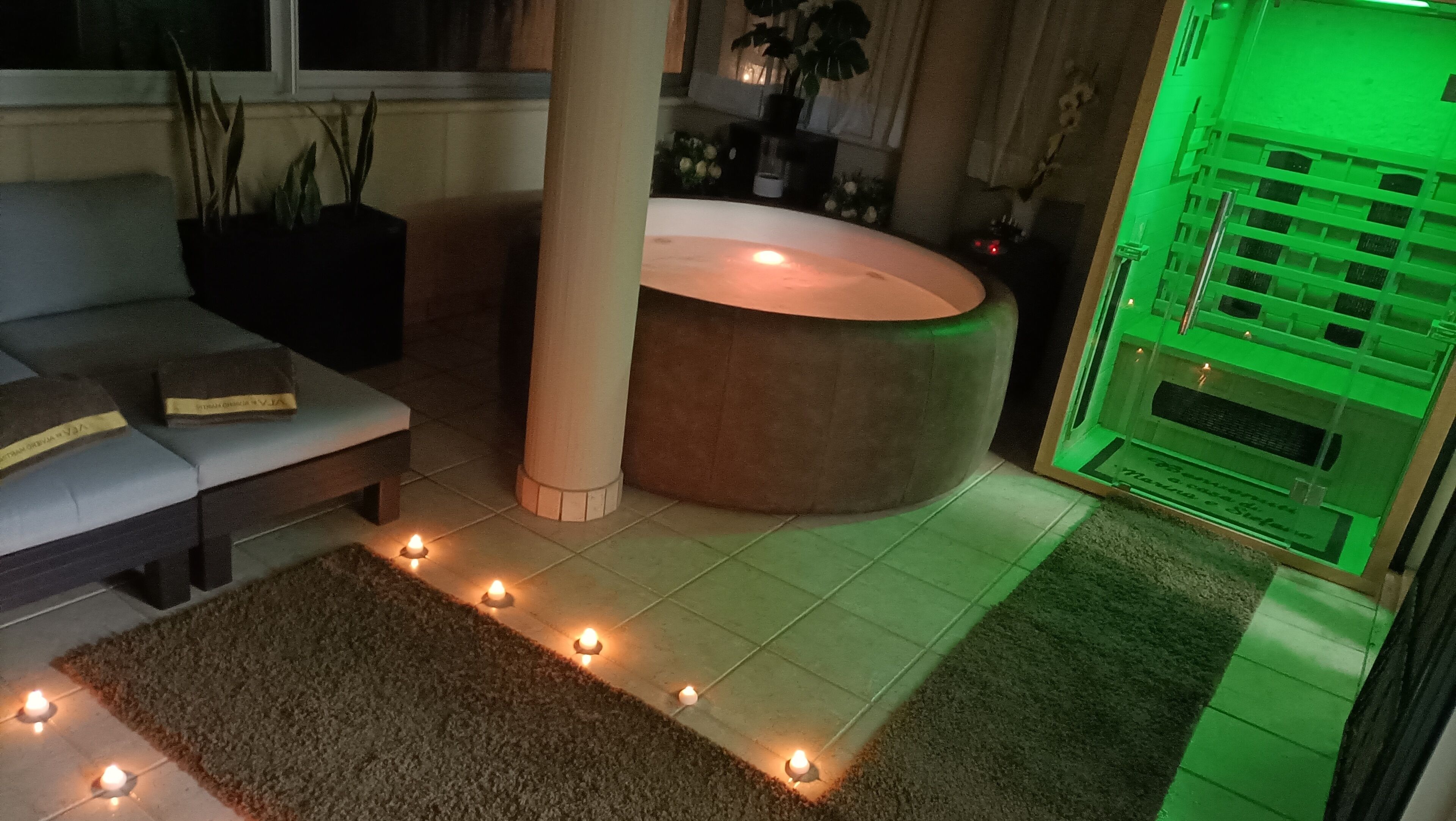 Ein Zimmer mit einer Couch, einer Säule, einer grün beleuchteten Zone und einer Reihe von Kerzen auf dem Boden.