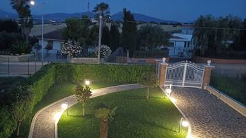 Un espace paysager aménagé en jardin, avec un chemin sinueux, un palmier et une entrée fermée par un portail.
