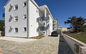 Un immeuble résidentiel à plusieurs étages, doté de balcons, d’une allée pavée et d’une voiture garée.