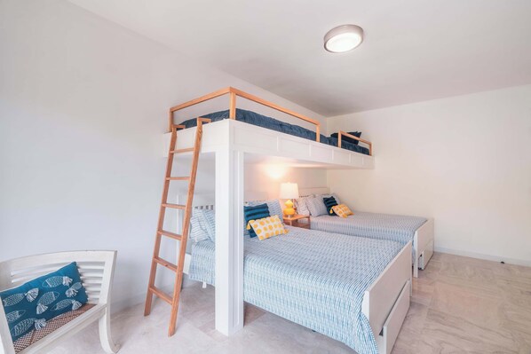 Un lit superposé avec une échelle en bois, une table de chevet avec une lampe et une chaise avec un coussin à motifs.