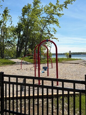A playground with red equipment, surrounded by trees and a body of water. - Cozy 3 BR family-friendly Home near Lake Couchiching (Severn)
