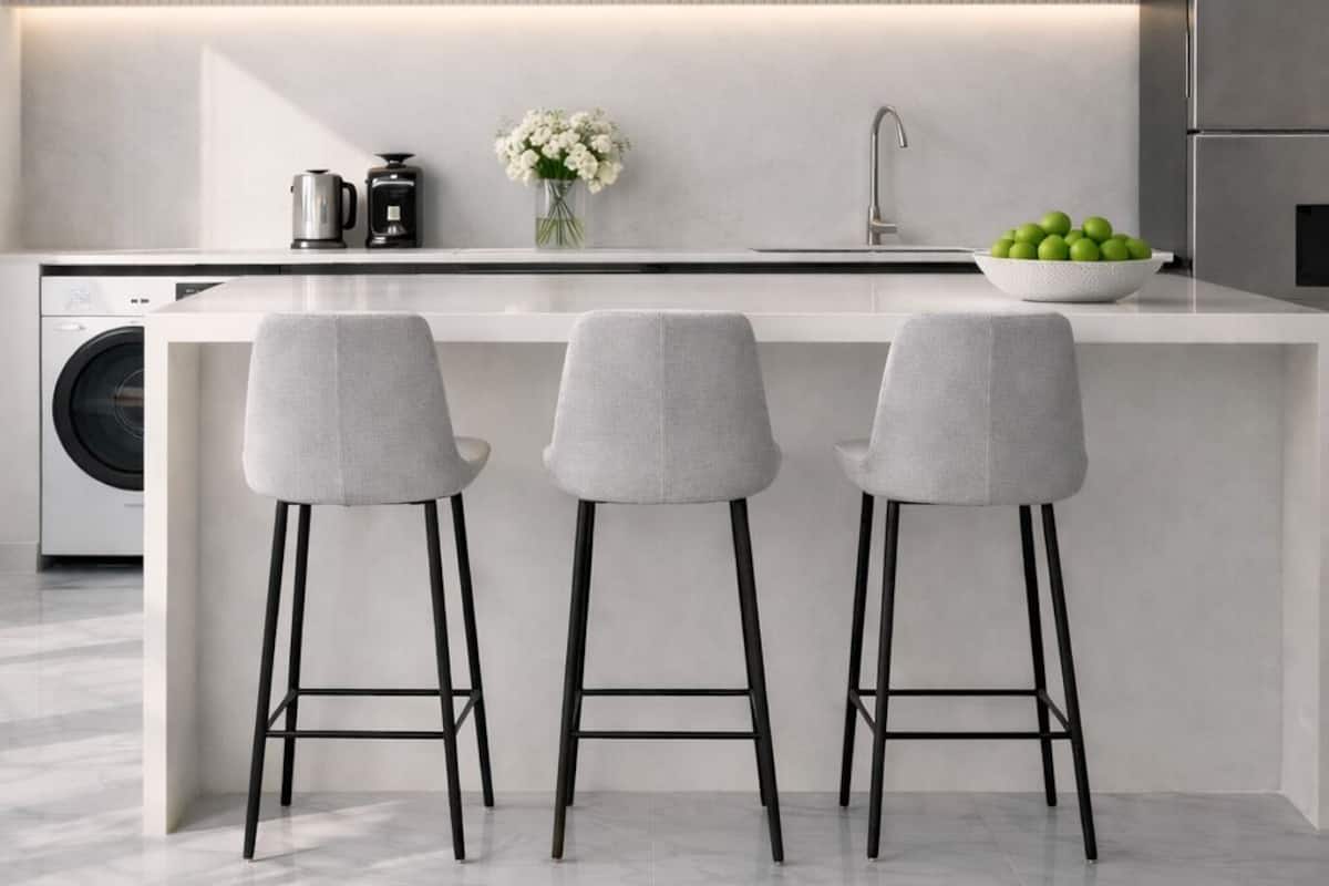 Cozinha moderna com ilha central, três banquetas, máquina de lavar e luminárias pendentes.