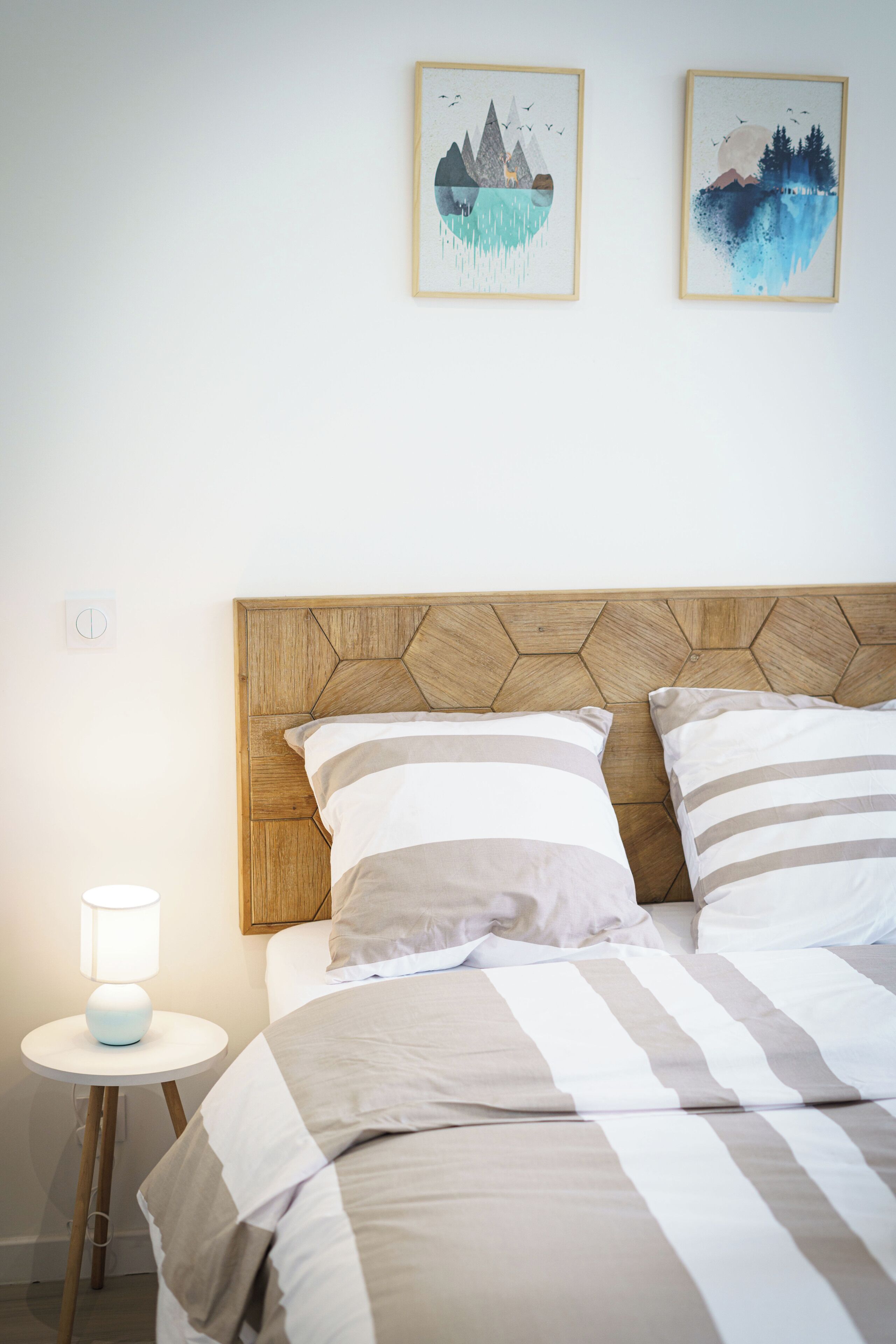Una cama bien tendida con ropa de cama a rayas, un cabecero de madera y dos obras de arte colgadas en la pared que representan escenas naturales.