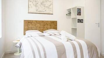 A bedroom with a bed, a wooden headboard, a map on the wall, a wardrobe, and a small table with a lamp.