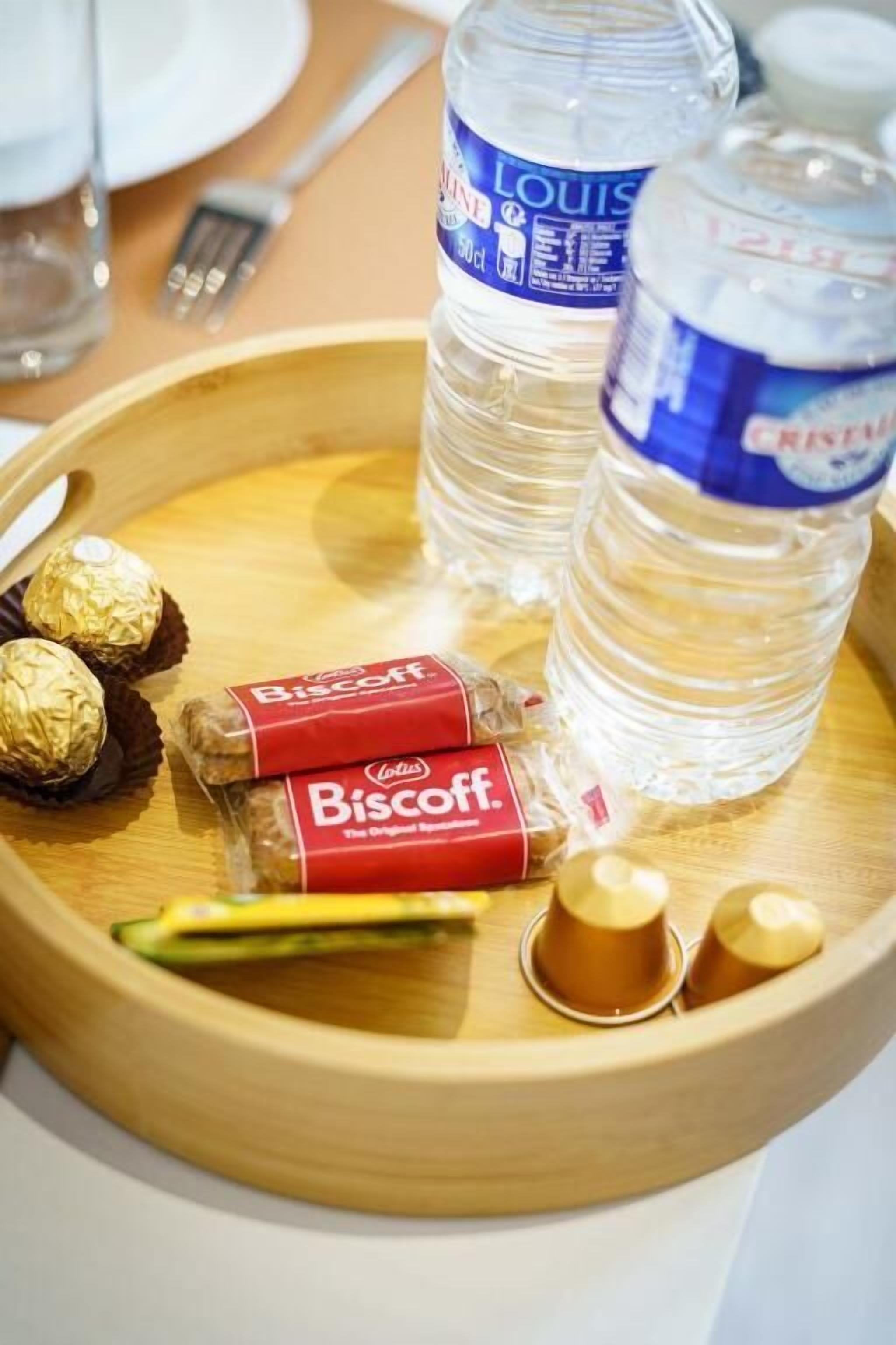 A wooden tray with two bottles of water, two chocolate-covered biscuits, and a small container of a beverage.