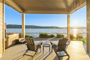 Une terrasse couverte avec deux fauteuils Adirondack et une petite table, d’où l’on peut admirer un plan d’eau et des collines lointaines.