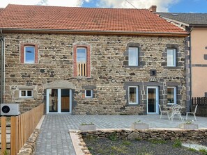 A stone building with a red-tiled roof, a wooden fence, and a paved patio area with outdoor furniture. - Le gîte à Théo - GELLES - Vacation Home (GELLES)