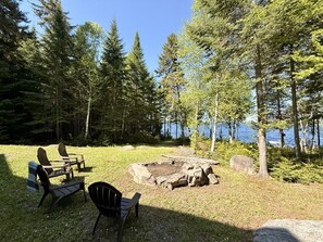 A lakeside campsite with a fire pit, chairs, and a view of the water.