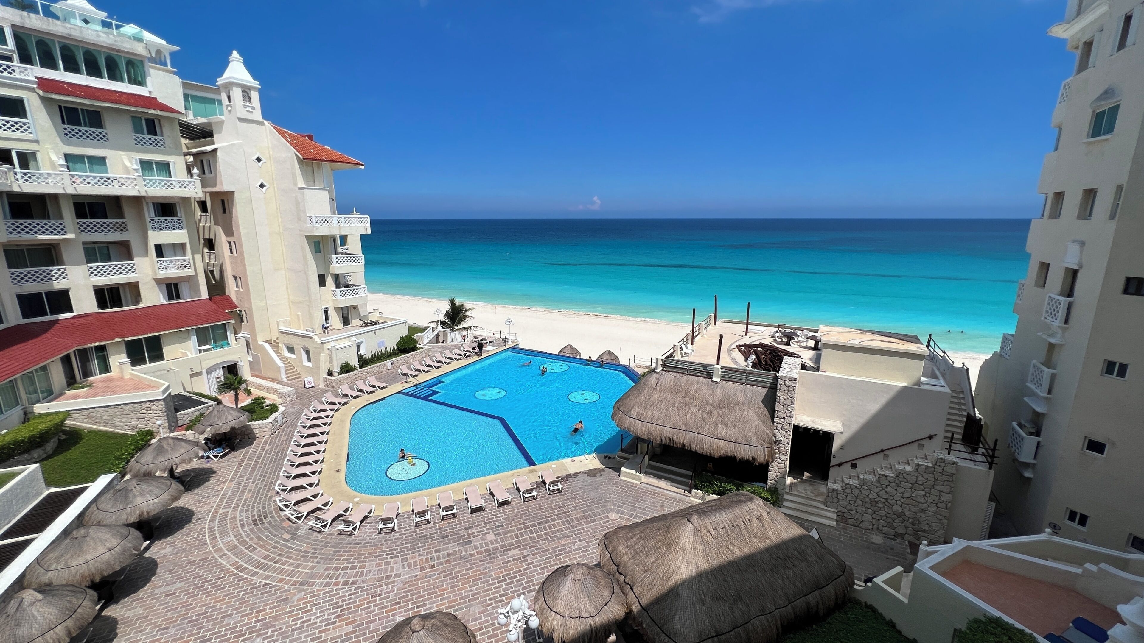 A resort with a swimming pool, beach, and hotel buildings.