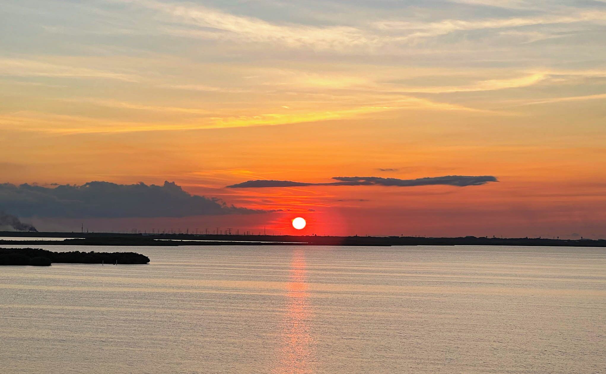A sunset over a calm body of water with a distant shoreline silhouette.
