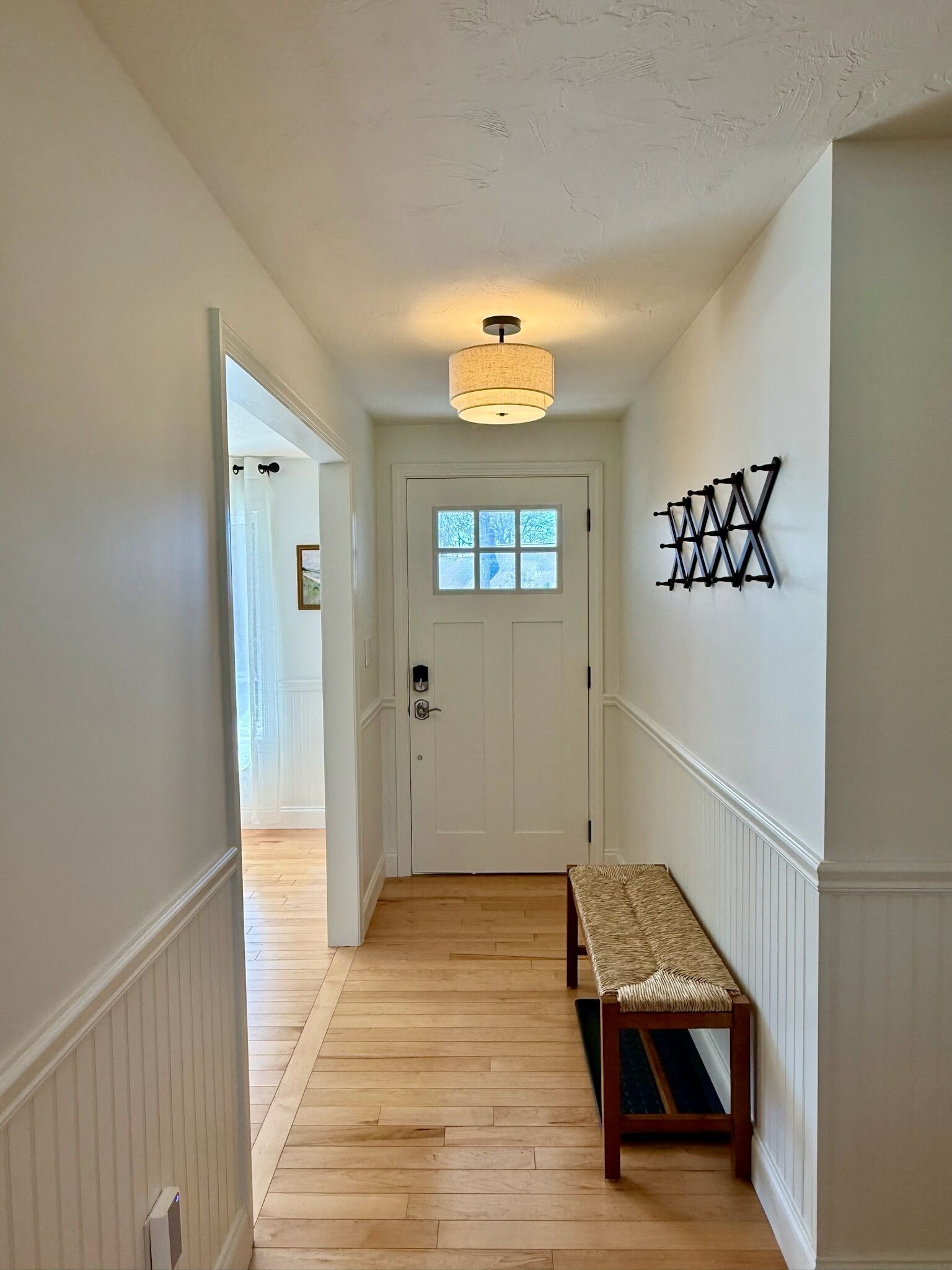 Un couloir doté d’un plancher en bois, d’un banc, d’une porte avec une fenêtre et d’un luminaire fixé au mur.