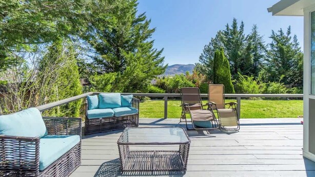 Une terrasse dotée de meubles en osier et d’une table en verre, entourée de verdure et baignée par un ciel dégagé.