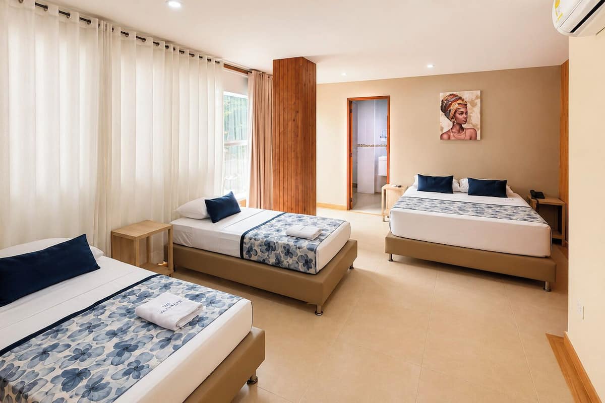 A hotel room with two beds, a wooden floor, a painting on the wall, and a window with curtains.