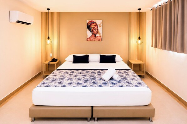 Habitació d'hotel moderna amb un llit gran, dues taules de nit, un aparell d'aire condicionat i un quadre a la paret.