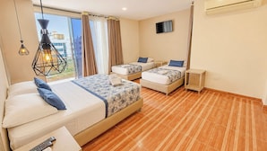 Habitación de hotel con dos camas, televisión, ventana con cortinas, ventilador de techo y un control remoto sobre una mesita.