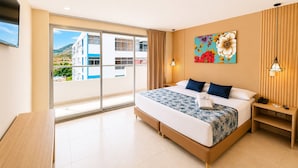 Habitación de hotel con una cama grande, vista a través de una puerta corredera, un cuadro en la pared y una mesita de noche con lámpara.