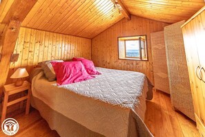 Ein Zimmer mit Holzboden, einem Bett, einem Nachttisch, einem Fenster und einem Kleiderschrank.