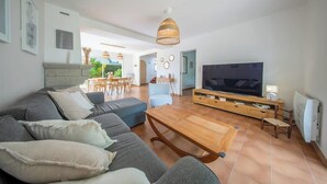 Een moderne woonkamer met een bank, televisie, houten salontafel en een eethoek.