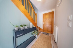 Ein Korridor mit einer Holztreppe, einem Konsolentisch mit Pflanzen, einem Heizkörper und einer Holztür.