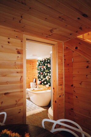 Ein Holzhütten-Interieur mit einem Badezimmer, das eine Badewanne und eine mit Blumen verzierte Wand zeigt.